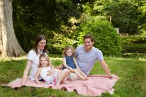 Portrait of mid adult parents and two daughters on picnic blanket in park — Stock Photo