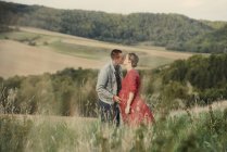 Romantic pregnant couple kissing in field — Stock Photo