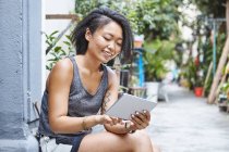 Жінка сидить на порозі в житлових провулку, дивлячись на цифровий планшет, Шанхай Французької концесії, Шанхай, Китай — стокове фото