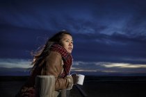 Junge Frau in Schal gehüllt schaut in der Abenddämmerung vom Strand aus — Stockfoto