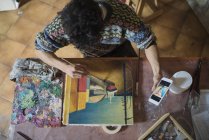 Artiste regardant smartphone tout en peignant sur toile en studio — Photo de stock
