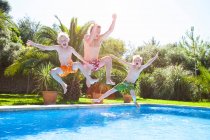Отец и сыновья в воздухе прыгают в открытый бассейн — стоковое фото
