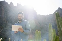 Jovem caminhante do sexo masculino olhando para tablet digital no vale iluminado pelo sol, Las Palmas, Ilhas Canárias, Espanha — Fotografia de Stock