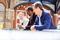 Three mature men at train station, standing together, talking — Stock Photo
