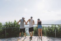 Vista trasera de tres amigos adultos jóvenes con vistas al lago de Como desde el balcón, Como, Lombardía, Italia - foto de stock