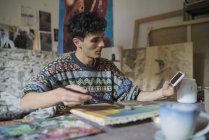 Artista masculino olhando para smartphone enquanto pinta em tela em estúdio — Fotografia de Stock