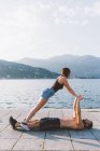 Young woman balancing with boyfriend lying on waterfront, Lake Como, Lombardy, Italy — Stock Photo