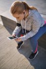 Изогнутая молодая женщина сидит на стене со смартфоном — стоковое фото
