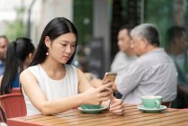 Femme d'affaires assise à l'extérieur, au café, en utilisant un smartphone — Photo de stock