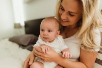 Baby girl sitting on mother's lap on bed — Stock Photo