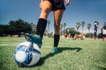 Cintura abajo de adolescente escolar jugador de fútbol con pie en la pelota en el campo de deportes de la escuela - foto de stock