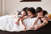Mãe, filho e filha deitados na cama, usando tablet digital — Fotografia de Stock
