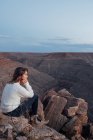 Mujer joven sentada en las rocas y mirando a la vista, Mexican Hat, Utah, EE.UU. - foto de stock