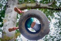 Vista de ángulo bajo del niño jugando en el columpio de neumáticos en el jardín - foto de stock