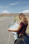 Femme penchée contre la voiture regardant la carte sur la route — Photo de stock