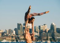 Teenage girl and young man, outdoors, woman balancing on man's hands in yoga position — Stock Photo