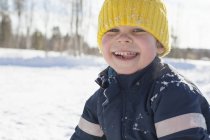 Portrait of happy boy in yellow knit hat in snow covered landscape — Stock Photo