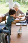 Grandmother and grandson sitting at table, using laptop — Stock Photo
