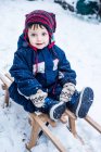 Портрет мальчика в лыжном костюме на санках — стоковое фото