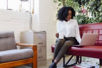 Afro-americana donna in ufficio seduta sul divano con computer portatile — Foto stock