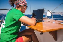 Giovane donna digitando sul computer portatile a bordo di yacht vicino alla costa, Croazia — Foto stock