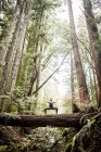 Young woman practicing yoga on top of log in forest — Stock Photo