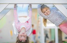 Girls at preschool, portrait climbing and upside down on climbing frame in garden — Stock Photo