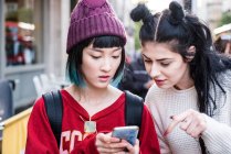 Дві молоді стильні жінки дивляться на смартфон на міській вулиці — стокове фото