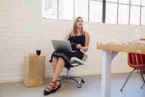 Mulher de negócios caucasiana em cadeira de escritório usando laptop — Fotografia de Stock