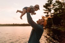 Man holding up baby daughter at lakeside — Stock Photo