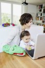 Mother holding baby girl on lap and using laptop — Stock Photo