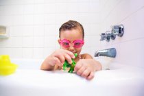 Girl wearing swimming goggles playing with toys in bath — Stock Photo