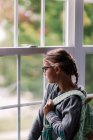 Девушка с рюкзаком смотрит в окно дома — стоковое фото
