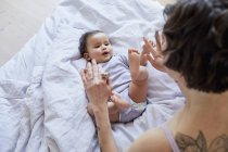Baby girl lying on bed and playing with mother — Stock Photo