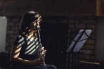 Girl with music stand playing on clarinet by fireplace — Stock Photo