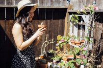 Mujer joven al aire libre, que tiende a plantas en maceta en el jardín - foto de stock