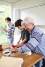Бабушка и внук готовят еду на кухне, мать на заднем плане — стоковое фото