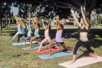 Colegialas practicando yoga guerrero una pose en el campo de deportes de la escuela - foto de stock