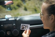 Over shoulder view of young woman on road trip holding instant photograph with boyfriend, Breckenridge, Colorado, USA — Stock Photo