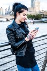 Молода жінка, дивлячись на смартфон на тисячоліття місток, Лондон, Великобританія — стокове фото