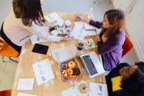 Vista de ángulo alto de colegas femeninos trabajando juntos y comiendo donas - foto de stock