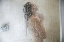 Young woman in shower behind steamed glass door — Stock Photo