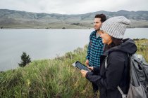 Couple hiking, standing beside Dillon Reservoir, young woman holding digital tablet, Silverthorne, Colorado, USA — Stock Photo