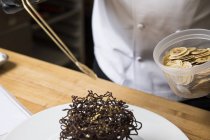 Chef placing slices of dried banana on chocolate nest cake decoration — Stock Photo