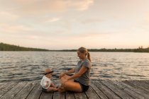 Mother sitting cross legged on lake pier with baby daughter — Stock Photo
