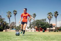 Adolescente colegiala patada pelota de fútbol en escuela campo de deportes - foto de stock