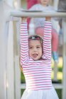 Girl at preschool, portrait hanging from climbing frame in garden — Stock Photo