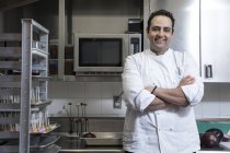 Retrato de chef en cocina comercial, brazos cruzados, mirando a la cámara sonriendo - foto de stock
