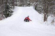 Man and son tobogganing down hill in snow covered forest — Stock Photo
