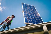 Two workmen preparing to install solar panel on roof of house, low angle view — Stock Photo